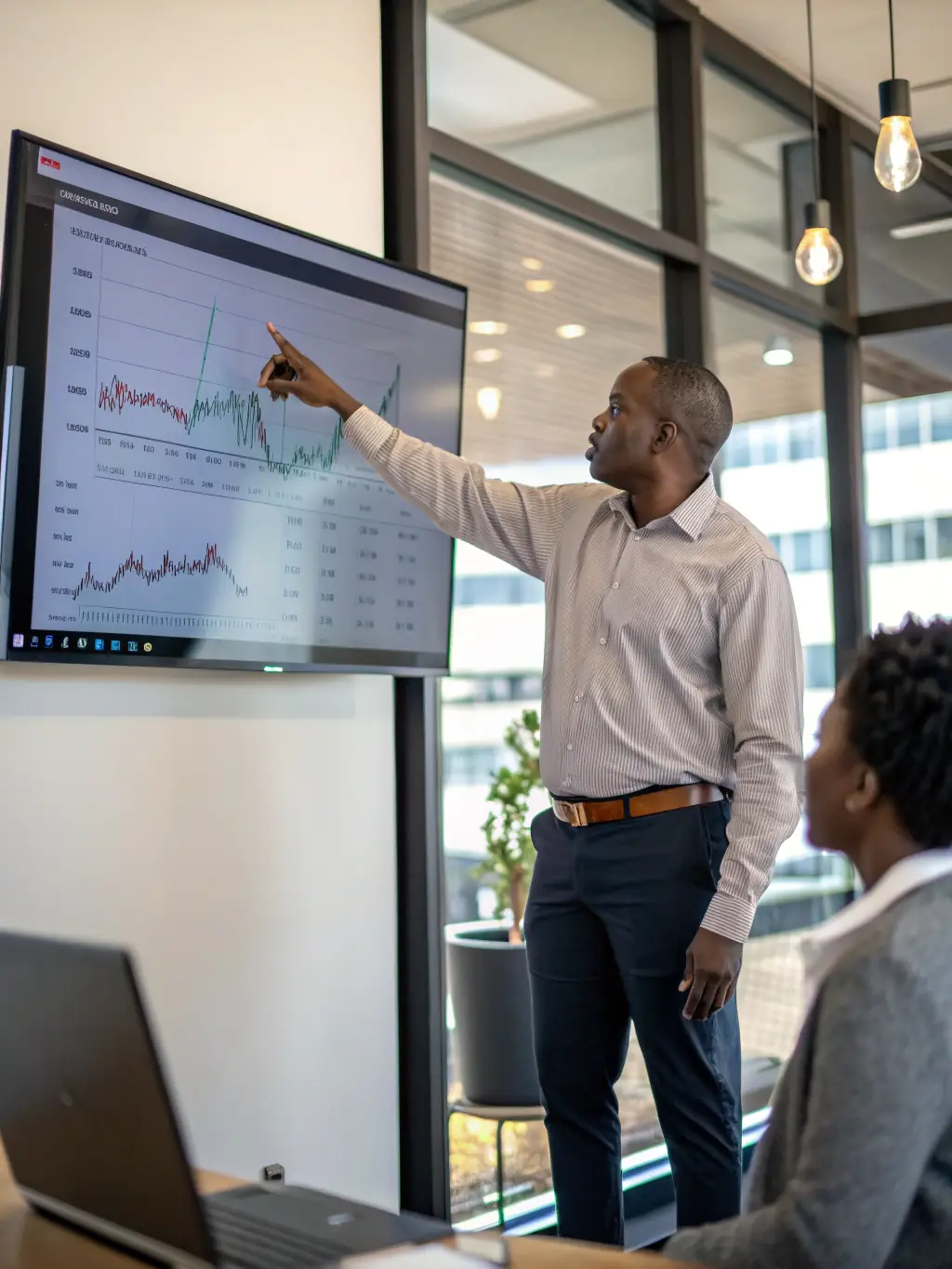 A professional advisor is presenting an investment strategy plan to a client in a modern office setting, with South African market data displayed on a screen in the background.